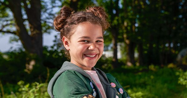Child actress Priya Rose smiling in an open field on a sunny day.